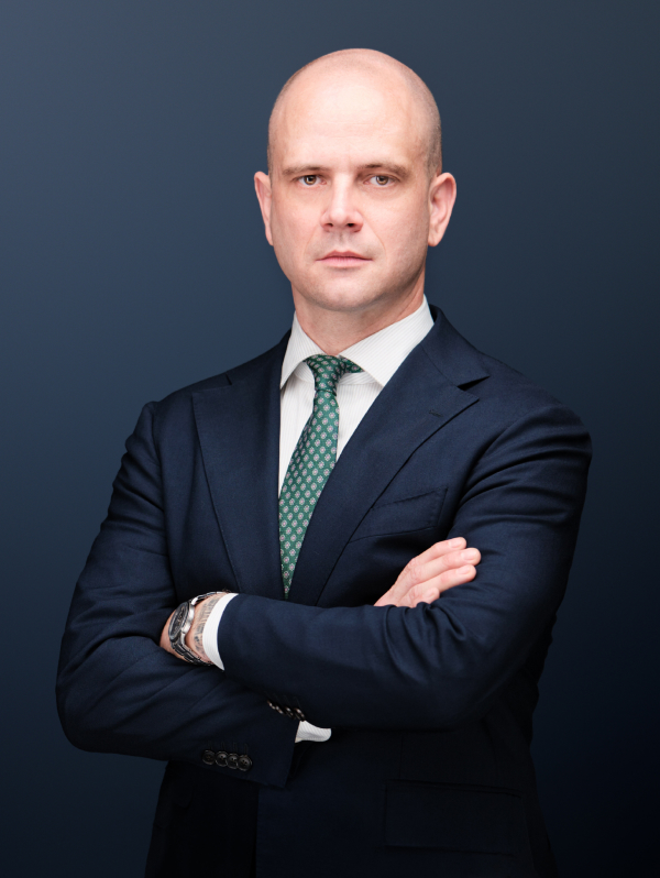 A St. Louis criminal defense attorney in a navy suit, white shirt, and green patterned tie, posing with his arms crossed.